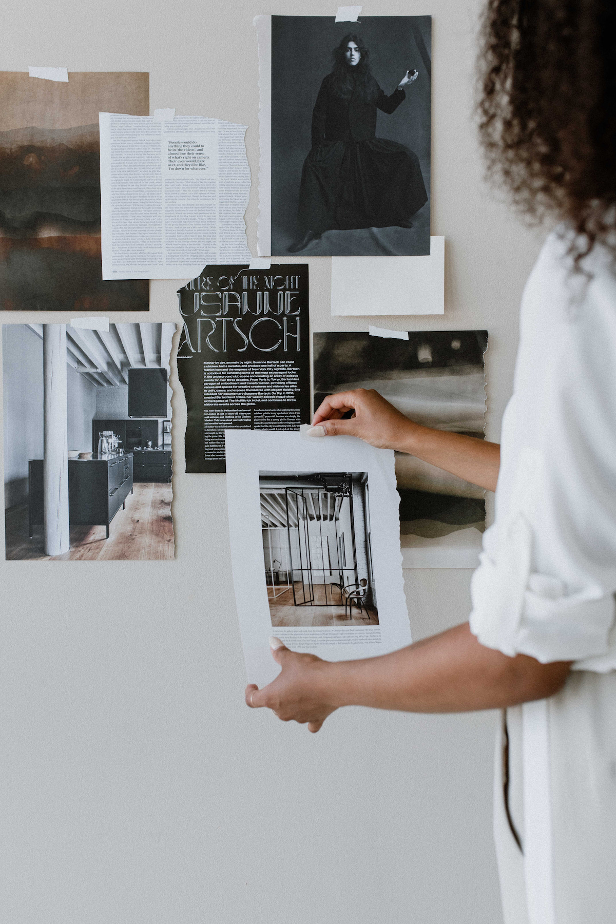 A person arranges a collection of monochrome and grayscale photographs and articles on a wall, showcasing artistic and architectural themes, illustrating the use of color psychology in branding.